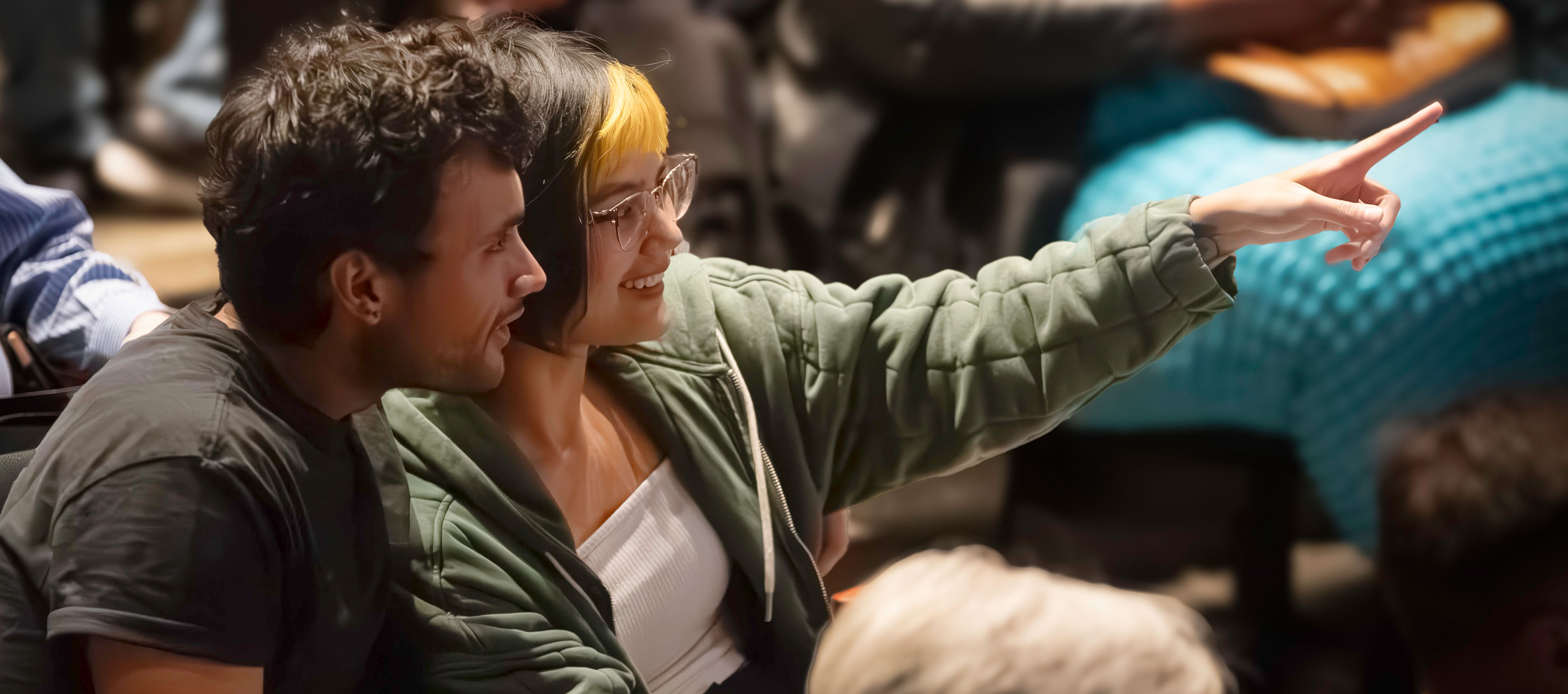 A young man and woman sit together in the theatre with the woman pointing toward the stage. (Photo by Allison Paraiso/Berkeley Rep)